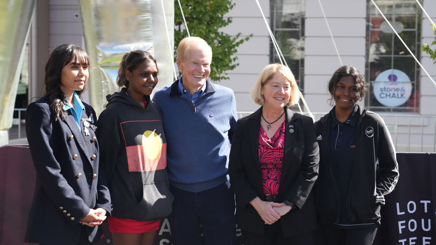 NASA Administrator Bill Nelson and Deputy Administrator Pam Melroy standing between three First Nations students in front of a building and signage.