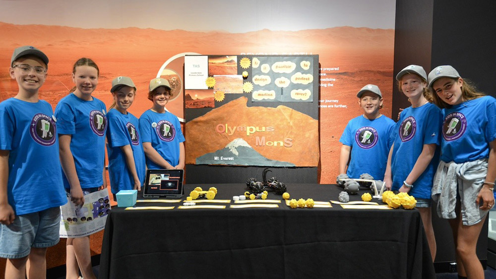 Lauderdale Primary School students in blue shirts pose either side of the table displaying their rover design presentation.