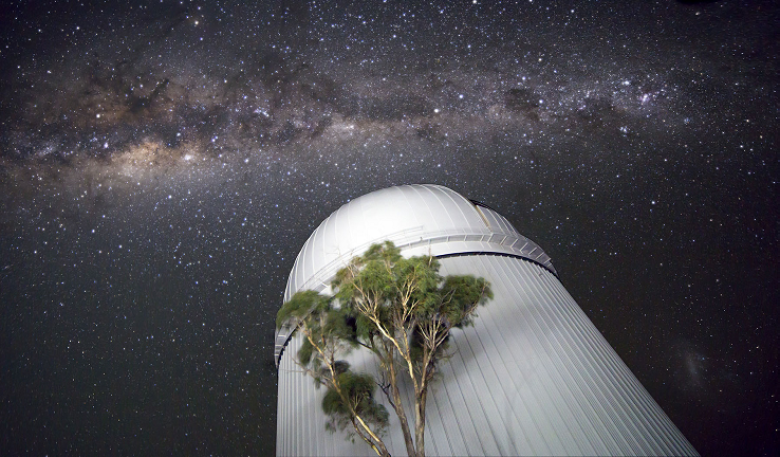 Astronomical observatory at night with view of galaxy behind.