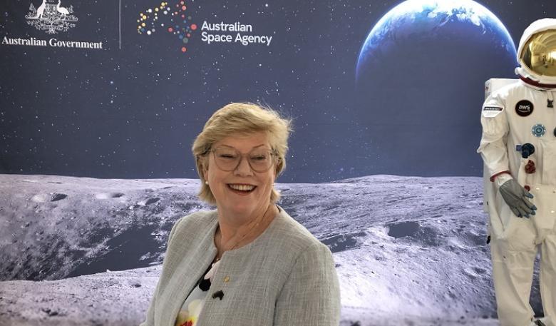 Portait of Head of Agency, Dr Megan Clark AC in front of a screen showing an astronaut on the moon facing with earth in the background.