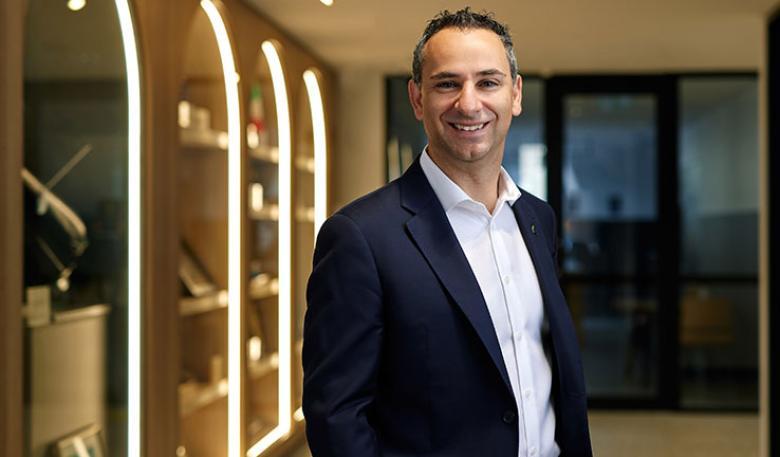 An upper body photo of the Head of the Australian Space Agency, wearing business attire. A space-related display in the background.