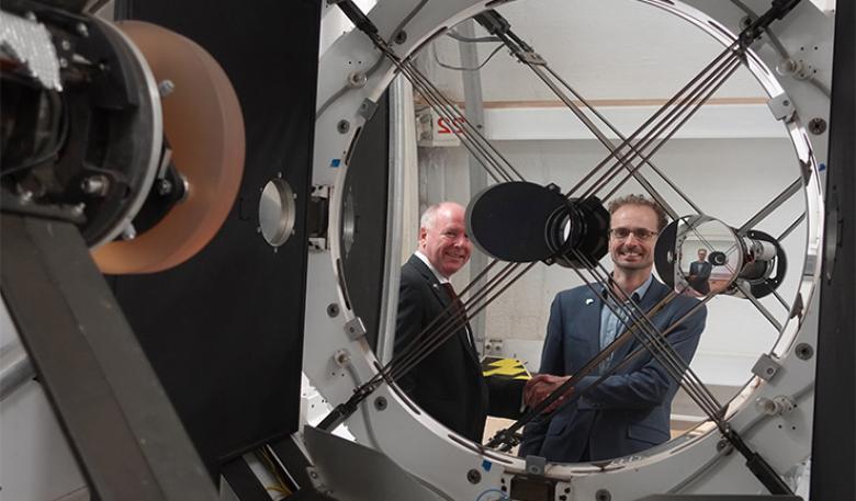 Australian Space Agency and EOS Space Systems leaders shake hands, reflected in the lens of space tracking equipment at the observatory.