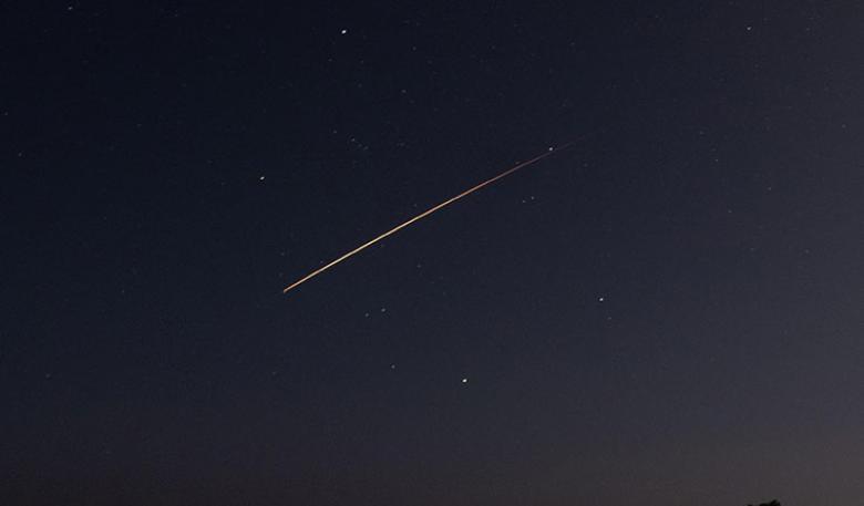 A fireball shoots across a dark sparsely stared sky