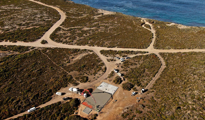 Birds-eye view of a rocket launch platform under construction and surrounding bush land by the sea.