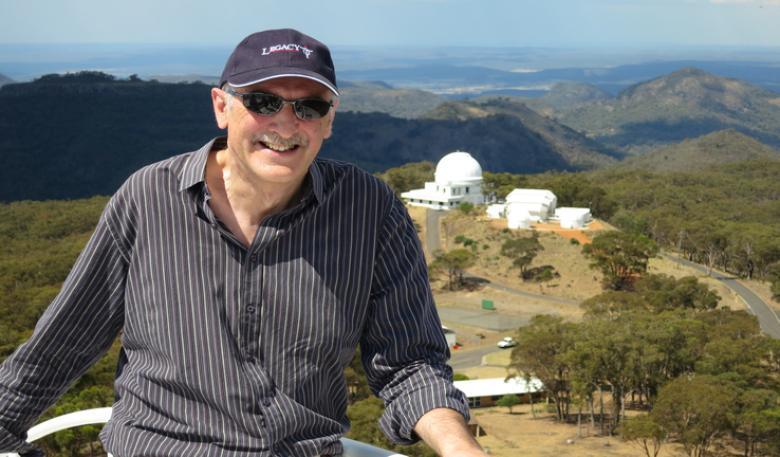 Astronomer-at-large, Fred Watson, poses for a photo with the Siding Spring Observatory at a distance in the background.