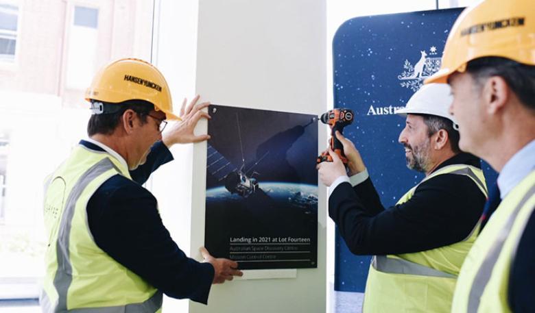 Three workers installing at a plaque of a satellite memorializing the opening of the centre