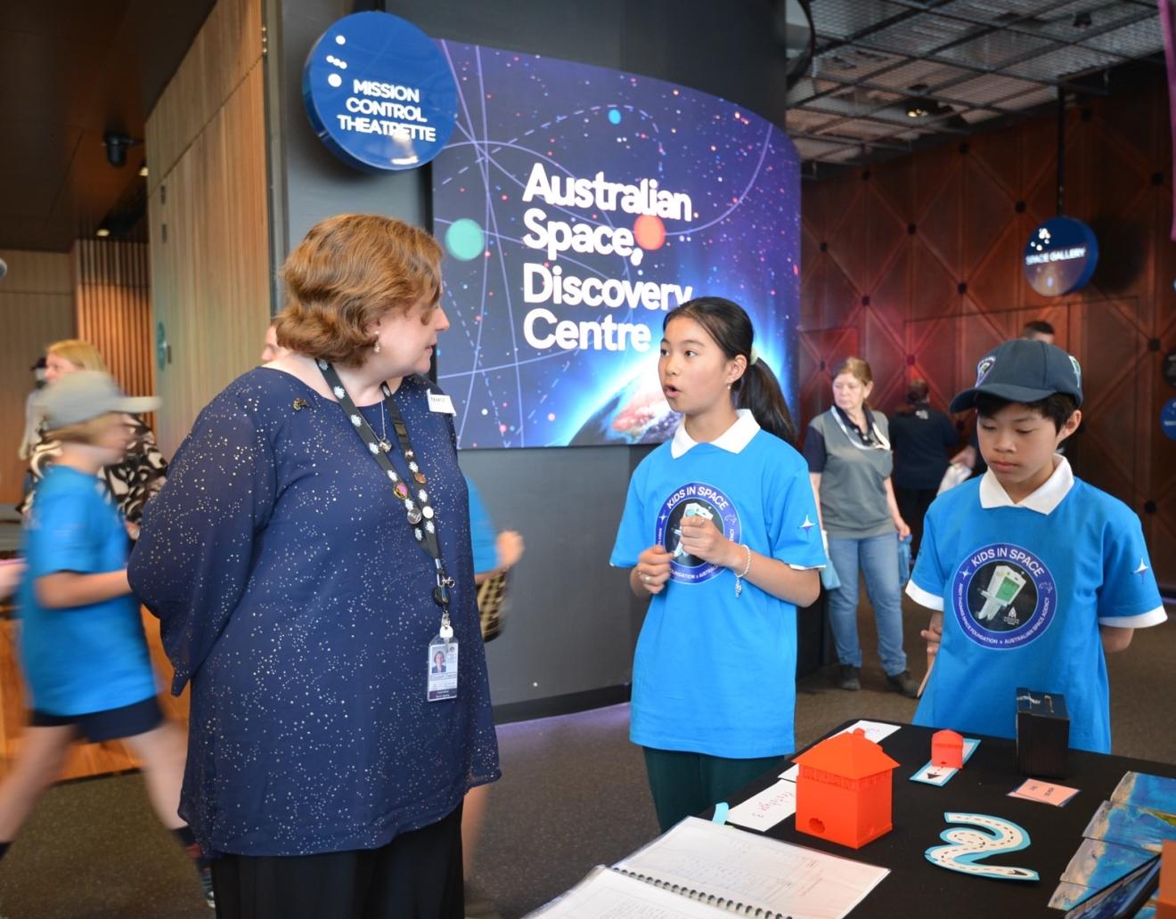 Young students and an adult standing next to a design concept.