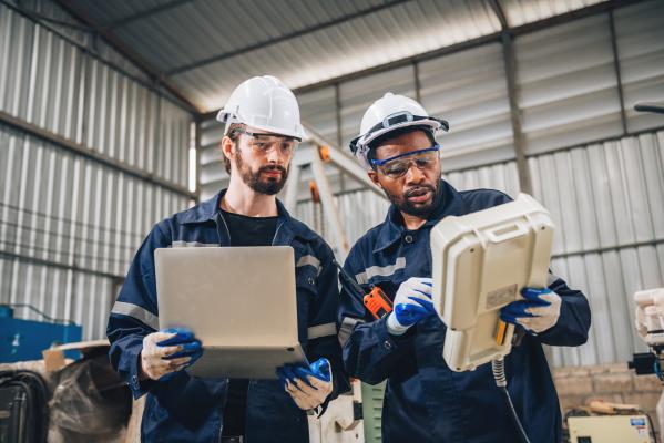 Two people in hard hats look at handheld display 