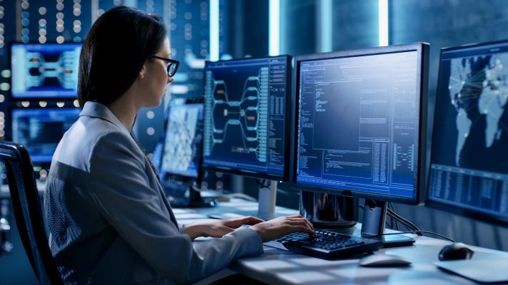 Systems engineer sits a modern desk with multiple screens