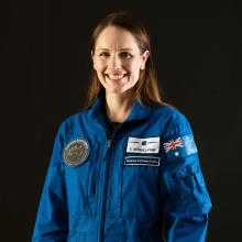 woman in an astronaut uniform smiling.