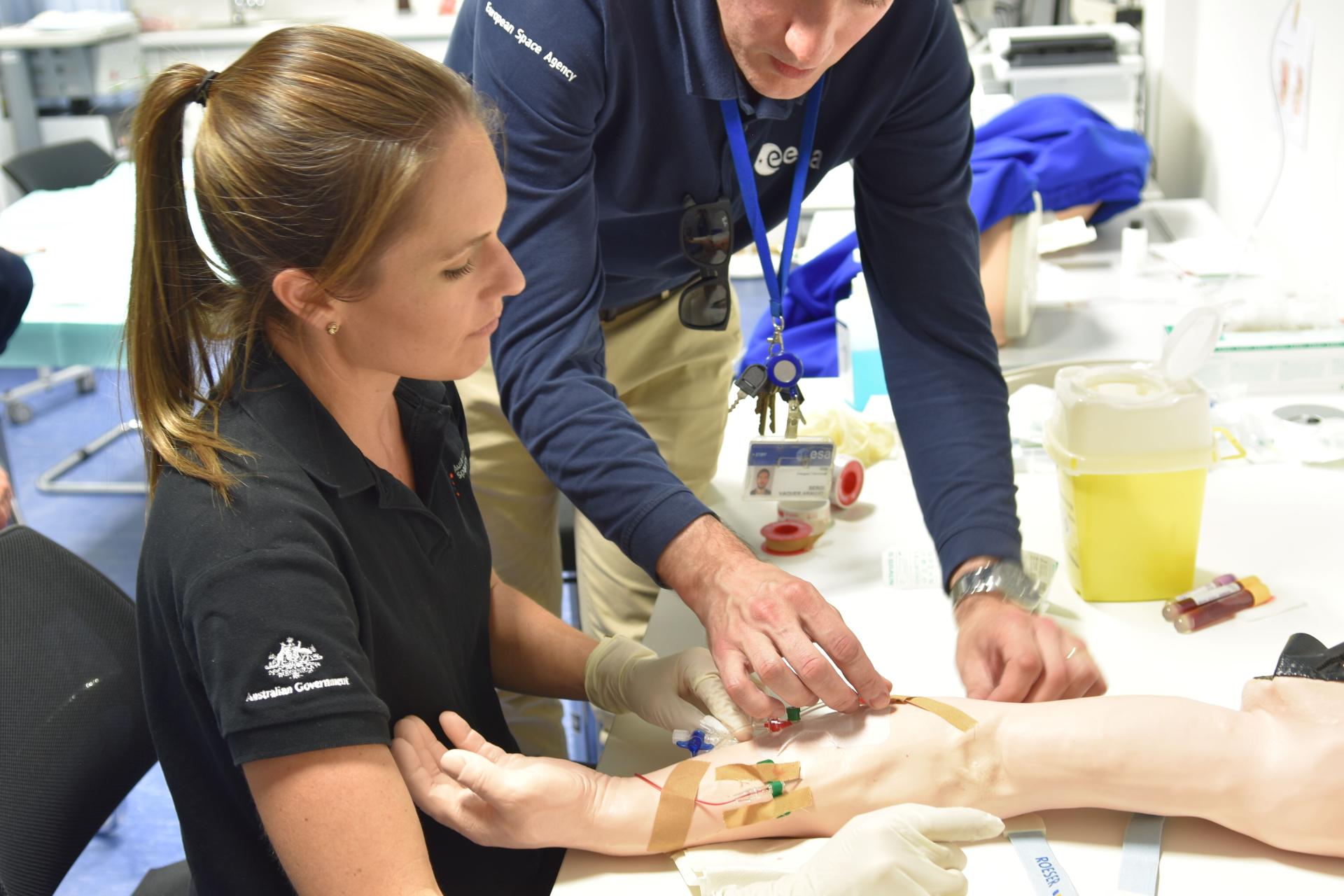 Two people practicing inserting a needle into a dummy arm.