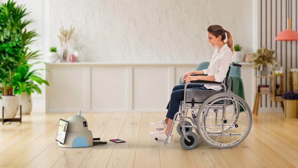 A small Akin robot on the left of the picture interacts with a person in a wheelchair on the right of the picture, inside the living room of a house